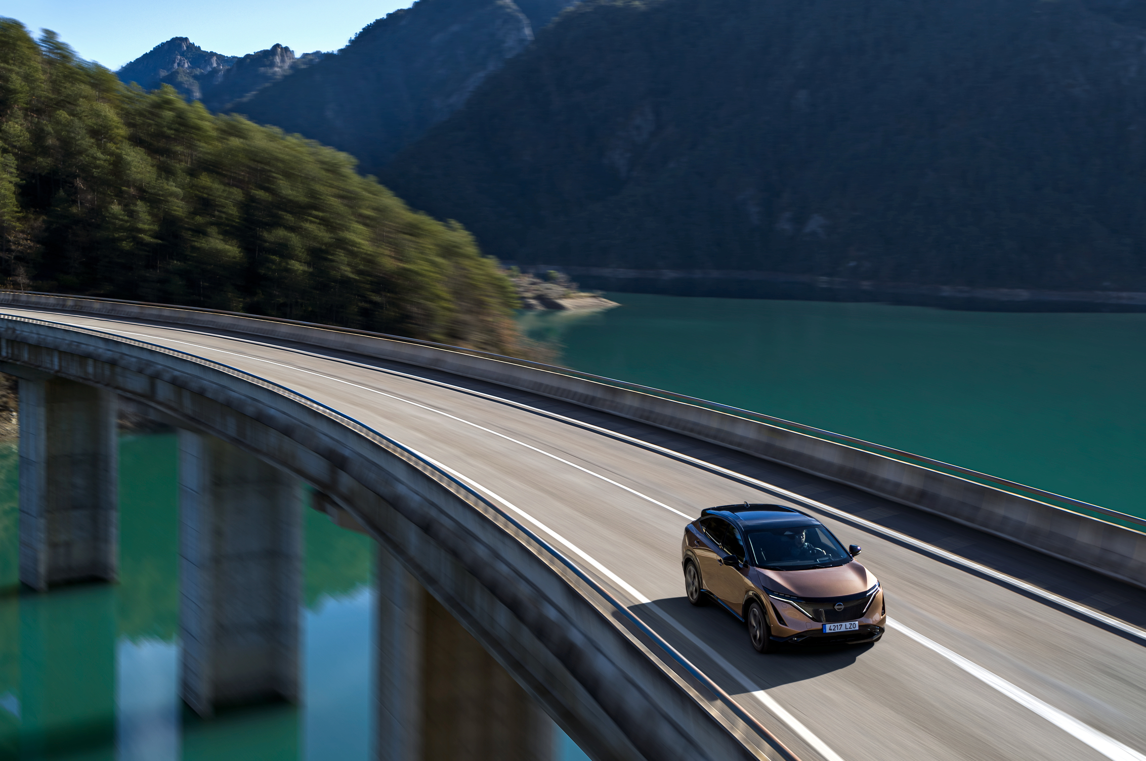 Vehículo Nissan Ariya 100% eléctrico circulando por carretera por encima de un embalse. 